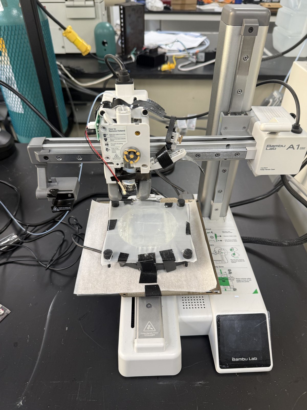 Bambu Lab A1 Mini desktop 3D printer converted into an ultrasonic spray-coating stage, with a sample taped to the bed
