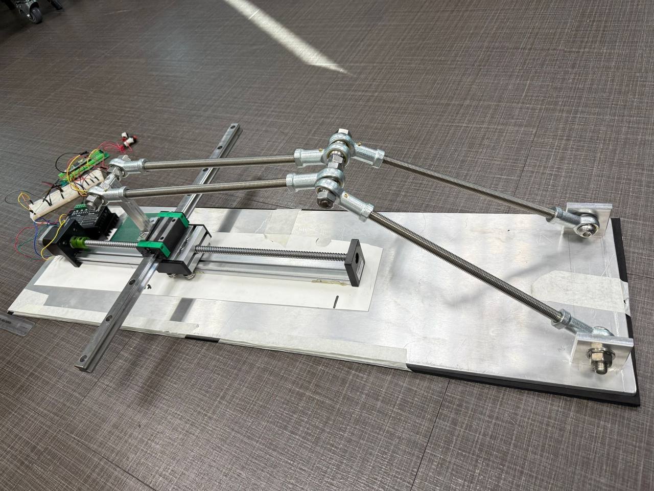 Early STRIDE prototype with a straight linear rail across the base, ball-screw slide and rod-end linkage
